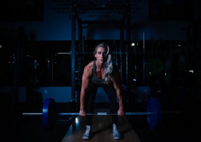 A fit woman lifting a barbell in a dimly lit gym, showcasing strength and determination.
