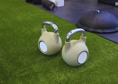 Two kettlebells on a green artificial grass floor in an indoor gym, ideal for strength training.
